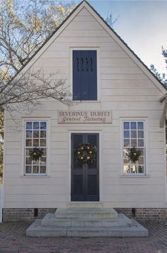 an old white building with wreaths on the front door and two windows in it