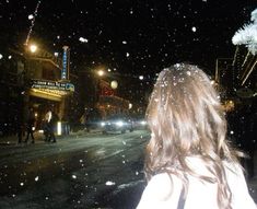 a woman standing in the middle of a street at night with snow falling all around her