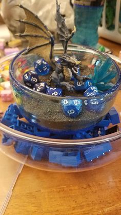 a bowl filled with blue and white dice sitting on top of a wooden table next to a toy dragon