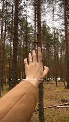 a person's hand reaching up into the air in front of trees with words written on them