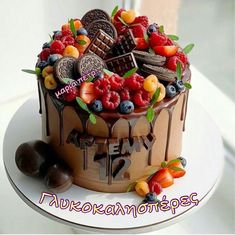 a cake decorated with chocolate, fruit and cookies on a white plate next to a window