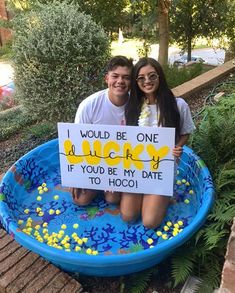 two people sitting in a pool holding a sign that says i would be one lucky if you be my date