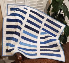 a blue and white quilt sitting on top of a chair next to a potted plant