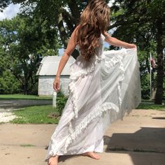 a woman in a white dress is walking down the sidewalk with her long flowing skirt