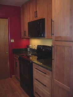 a kitchen with wooden cabinets and black appliances in it's center island, next to a red wall