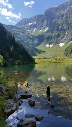 the mountains are reflected in the still water of this lake, with rocks and grass on both sides