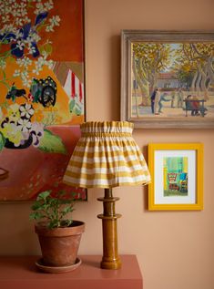 a lamp on a table next to a painting and potted plant in front of it