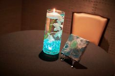 a glass vase with water and flowers in it next to a lit candle on a table