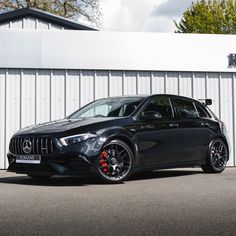 a black mercedes cla parked in front of a white building with red rims