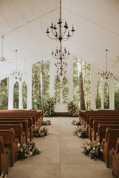 an outdoor wedding venue with rows of pews and chandeliers, decorated with flowers