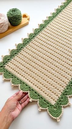 someone is crocheting a green and white afghan on a table next to some yarn