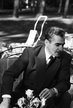 a man in a suit and tie sitting on a bench next to a flower bouquet