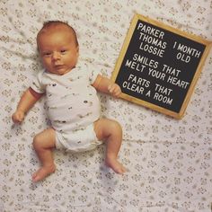 a baby laying on top of a bed next to a sign