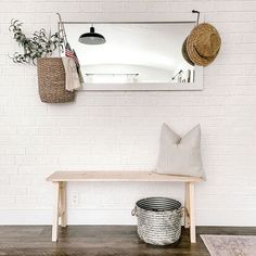 a wooden bench sitting under a mirror next to a white brick wall