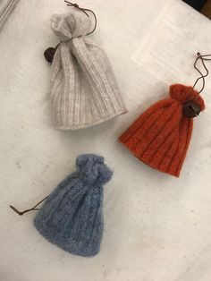 three knitted items are sitting on top of a white surface, one is orange and the other is blue