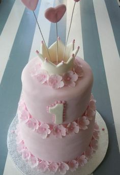 a pink cake with hearts on top and the number one is decorated in fondant