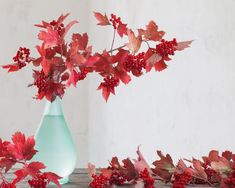 a vase filled with red leaves and berries sitting on top of a table next to another vase