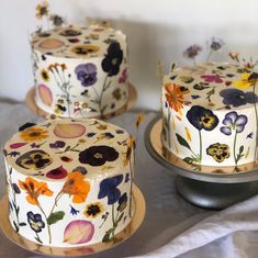 three cakes decorated with colorful flowers and leaves on top of each other, sitting on wooden platters