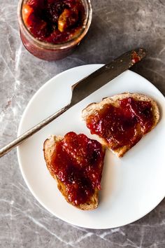 two pieces of bread with jam on them and a knife next to it, sitting on a plate