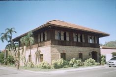 an old brick building sitting on the side of a road next to a palm tree