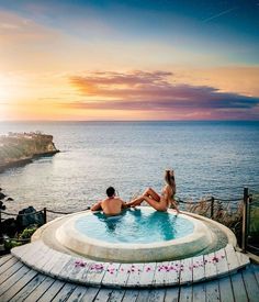 two people sitting in an outdoor hot tub overlooking the ocean at sunset or sunrise,