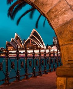 the sydney opera house is lit up at night with lights in the foreground and water behind it