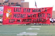 a group of people standing on top of a football field holding up a red banner