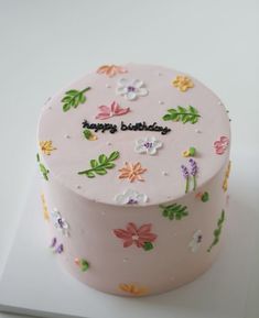 a pink birthday cake decorated with flowers and the words happy birthday on it's side