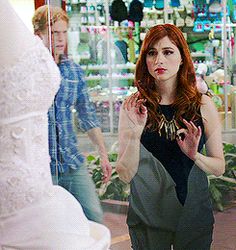 a woman standing in front of a wedding dress and looking at her reflection in the mirror