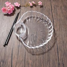 an empty glass bowl with chopsticks on a wooden table next to pink flowers