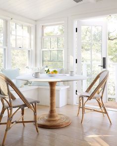 a table and chairs in a room with white walls, wood flooring and windows