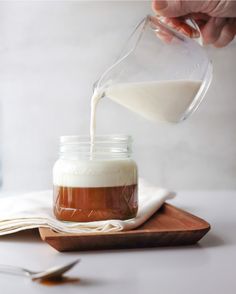 someone pouring milk into a jar on top of a wooden cutting board