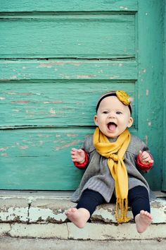 a baby wearing a yellow scarf sitting on the steps with its mouth open and tongue out