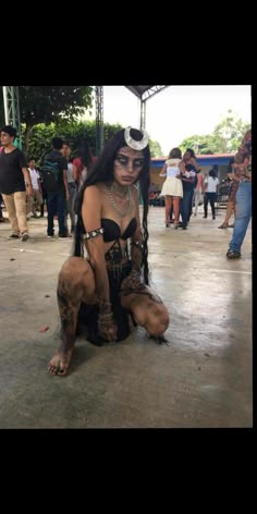 a woman dressed in costume sitting on the ground with other people around her and one person standing behind her