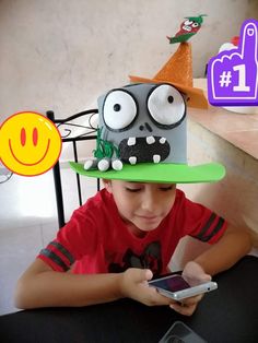 a young boy wearing a paper hat and holding a cell phone in front of him