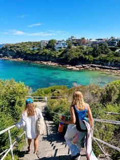 two women walking up stairs to the beach with clear blue water in the back ground