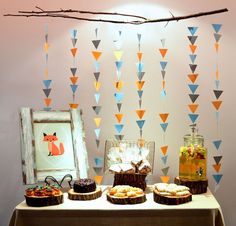 a table topped with cakes and pastries next to a wall covered in paper triangles