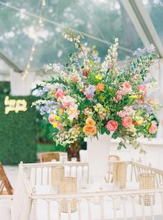 a vase filled with lots of colorful flowers on top of a white table covered in greenery