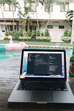 an open laptop computer sitting on top of a wooden table next to a swimming pool