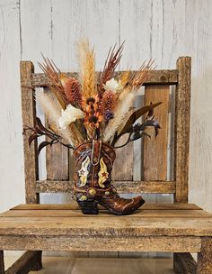 a cowboy boot with dried flowers and feathers sits on a bench in front of a wooden wall