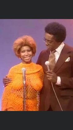 two people standing next to each other in front of a microphone and an orange dress