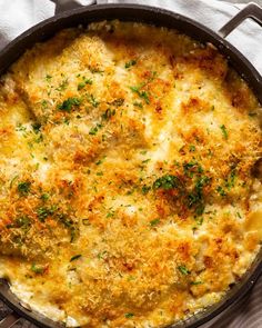 a casserole with cheese and herbs in a pan on a tablecloth next to utensils