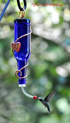 a hummingbird flying towards a blue bird feeder with a heart on it's side