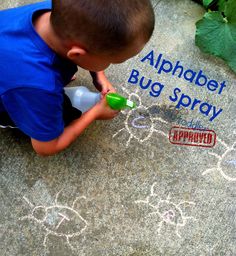 a young boy is drawing with chalk on the sidewalk and has an alphabet bug spray bottle in his hand