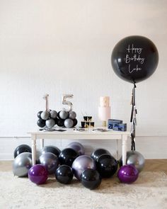 a birthday party with balloons, cake and other items on a table in front of a white brick wall