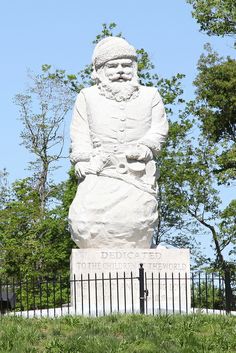 a large white statue sitting on top of a lush green field next to a fence