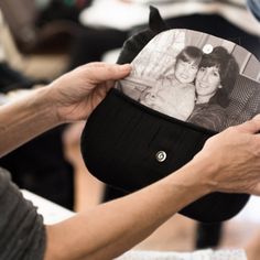 a person holding up a hat with a picture on it and another hand touching the cap