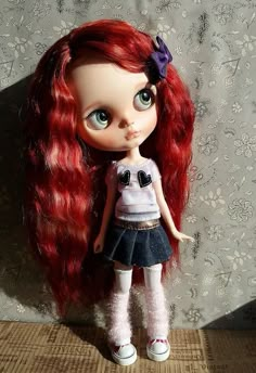 a doll with long red hair wearing a white shirt and black skirt is standing next to a wall