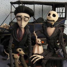 two figurines sitting next to each other in front of a car with skeletons on it