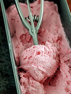 a scoop of pink ice cream in a green container with a metal tong on it